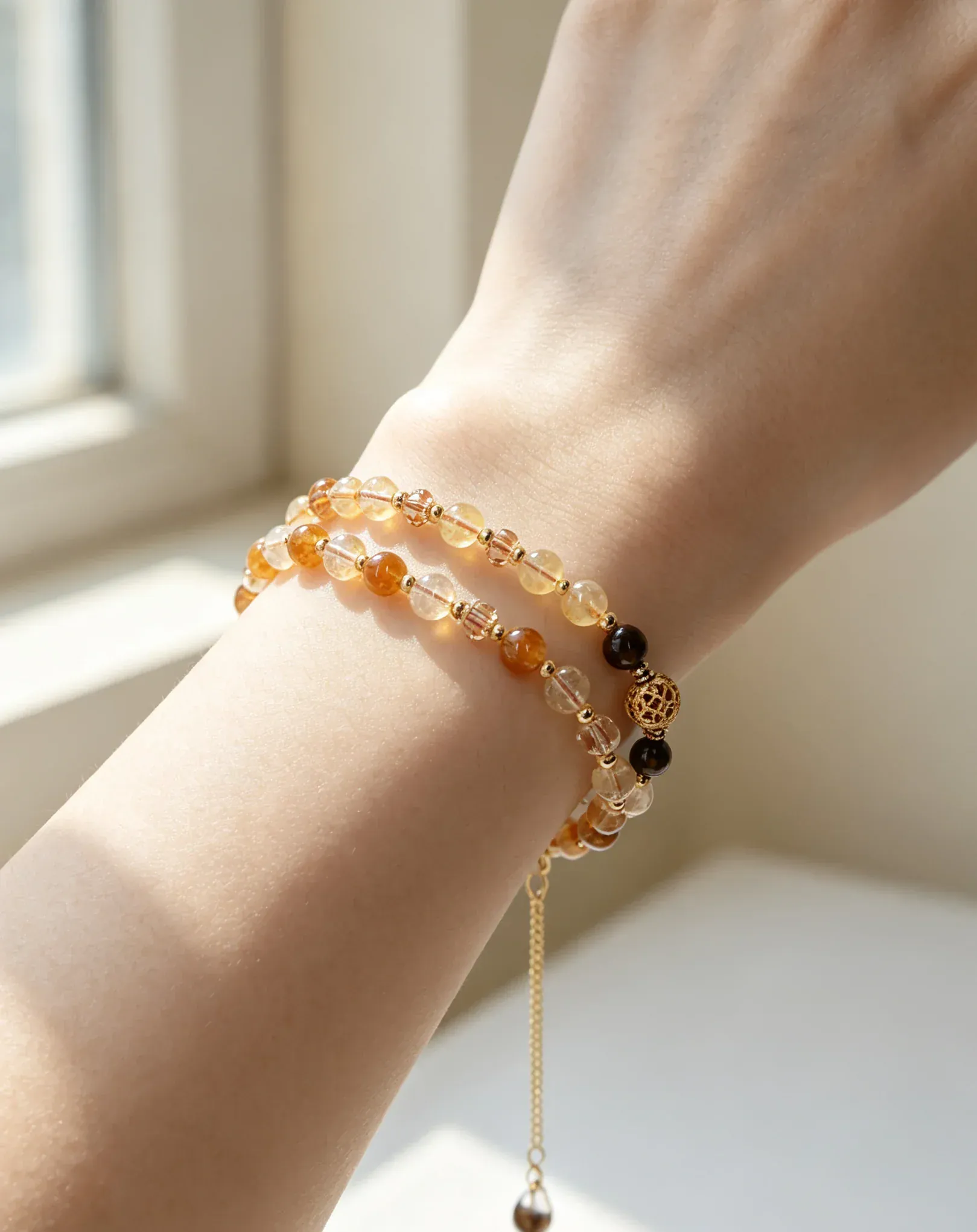 Hand wearing layered natural crystal bracelets with amber and gold beads, perfect for healing energy and style.