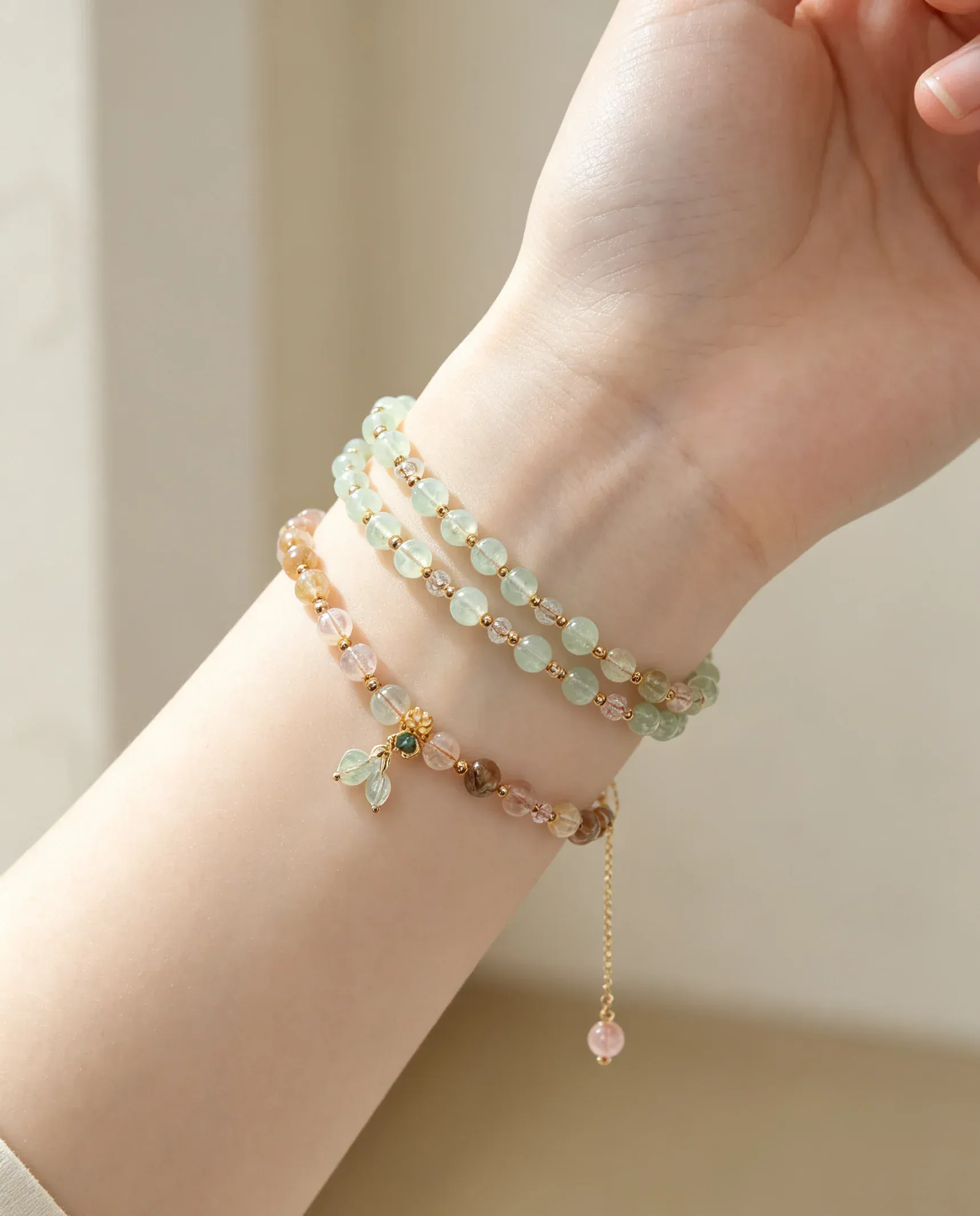 Hand wearing layered natural crystal bracelets with green, pink, and gold beads for positive energy