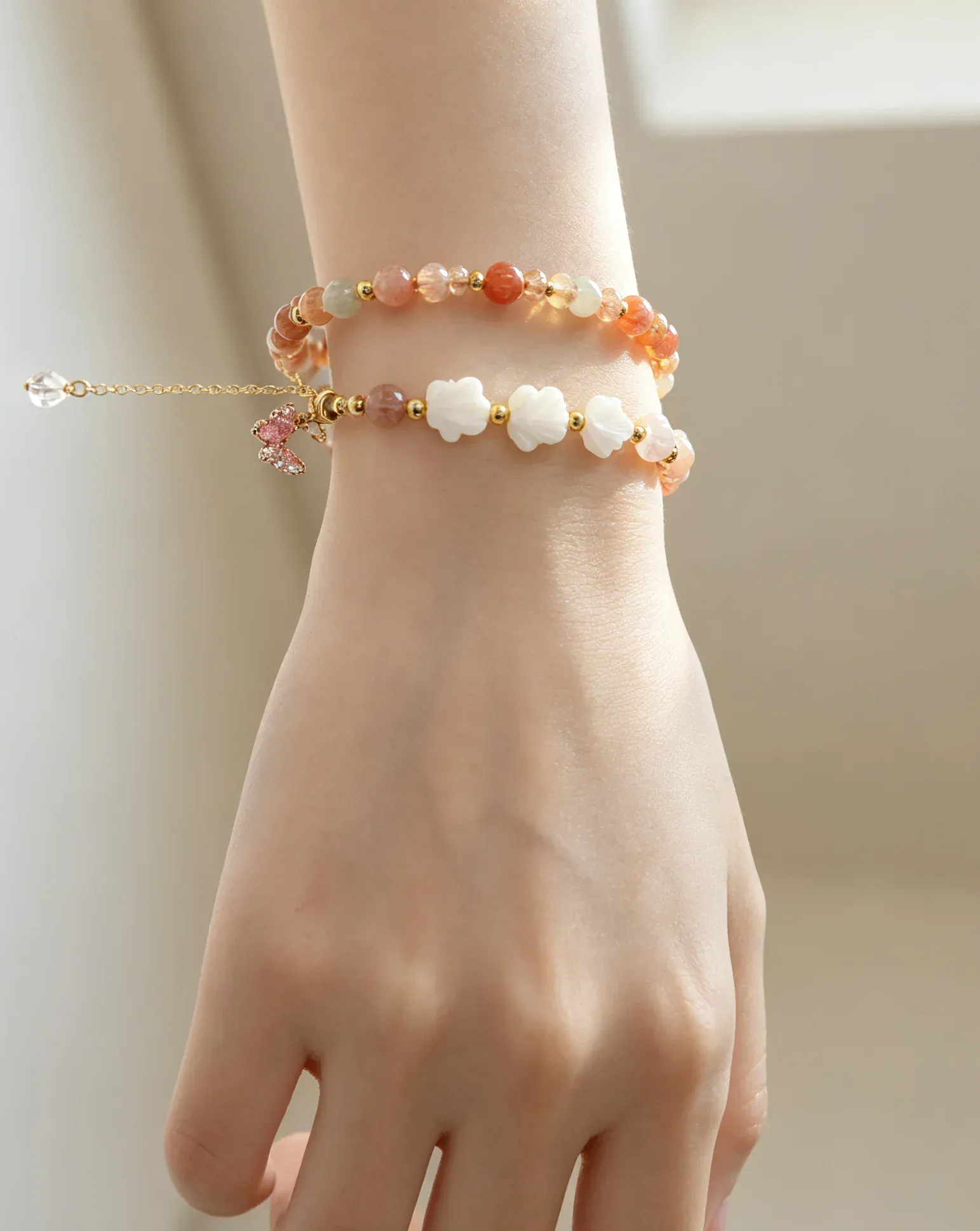 Hand wearing two natural crystal bracelets with flower beads and gold accents, perfect for positive energy and healing.