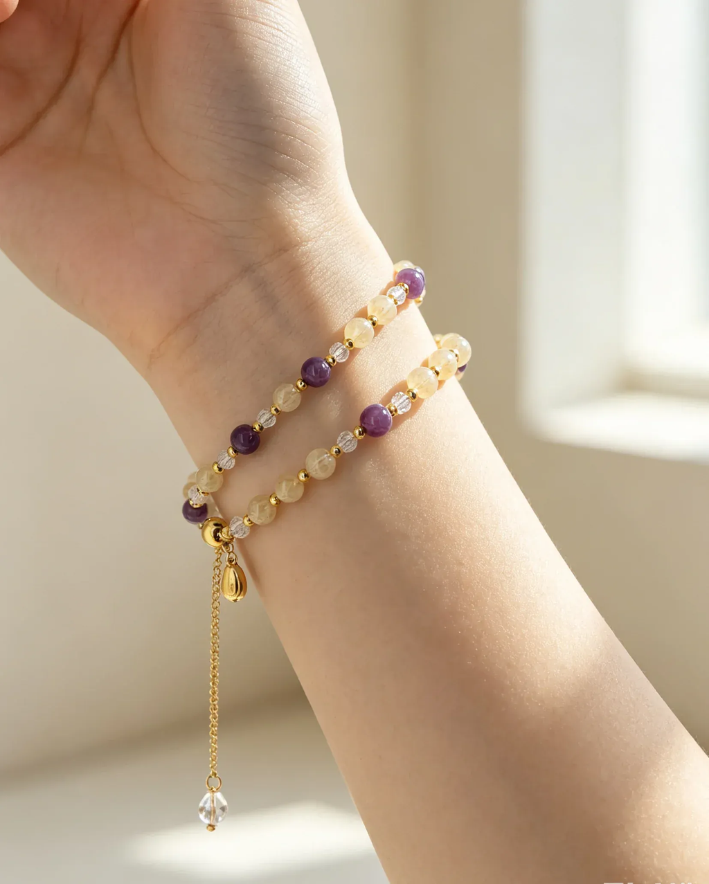 Hand wearing natural crystal bracelet with purple and gold beads, healing gemstone accessory for women