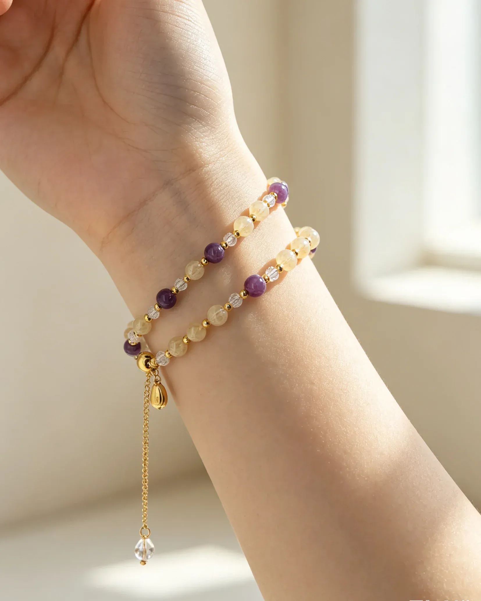 Hand wearing natural crystal bracelet with purple and gold beads, healing gemstone accessory for women