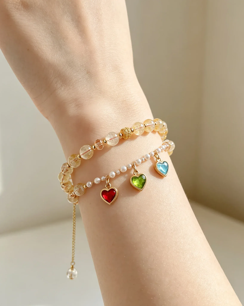 Layered crystal bracelets with heart charms in red, green, blue on woman's wrist, natural gemstone jewelry