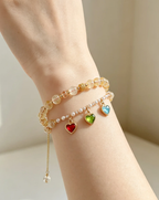 Layered crystal bracelets with heart charms in red, green, blue on woman's wrist, natural gemstone jewelry