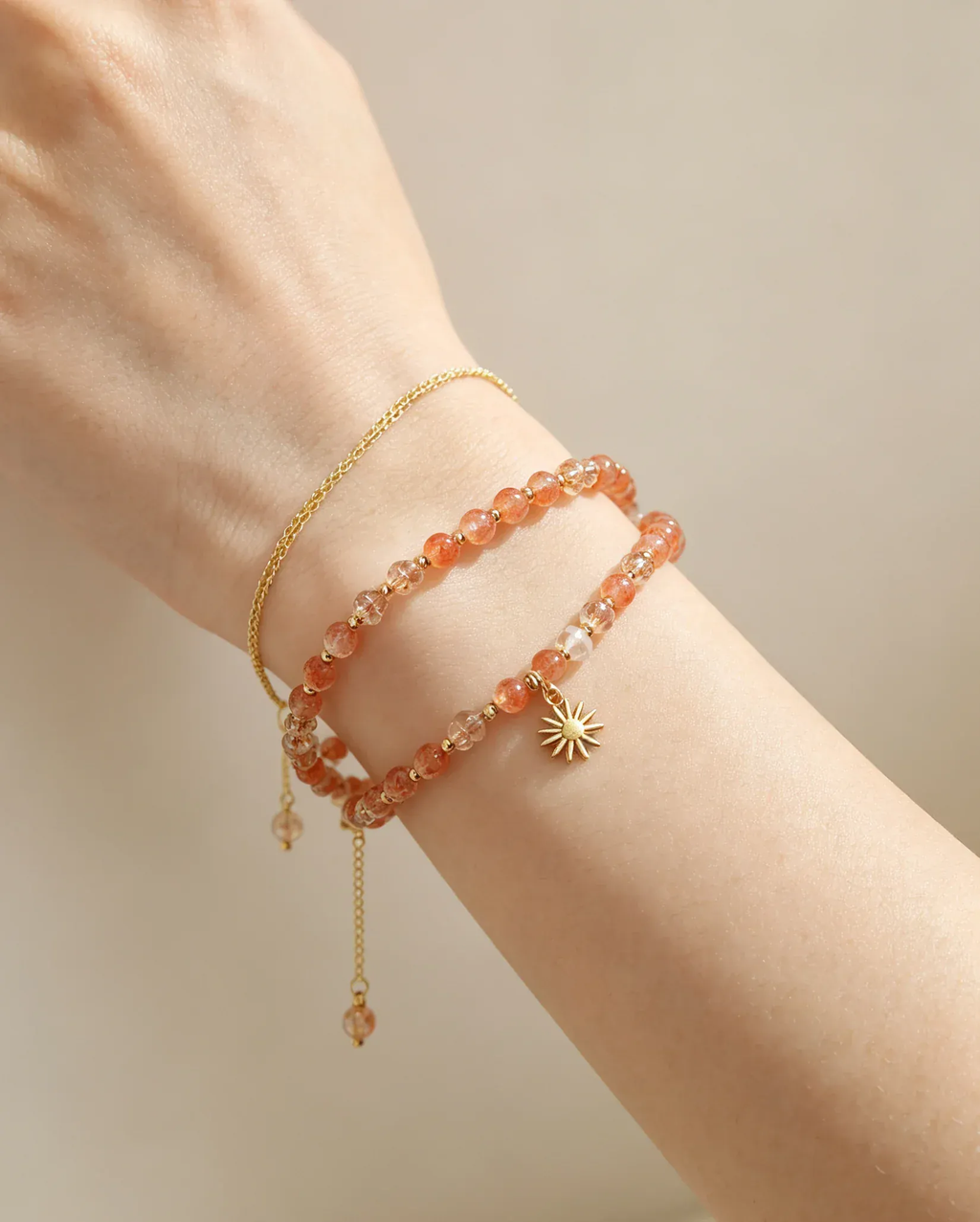 Hand wearing layered natural crystal bracelets with sun charm, healing gemstone accessories for women